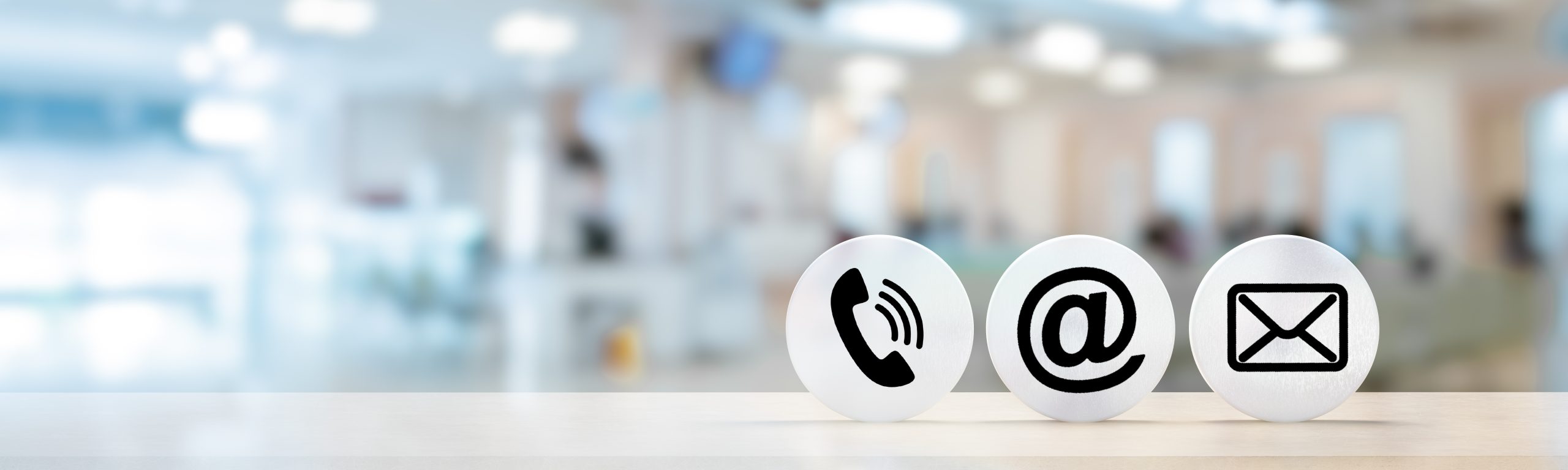 Contact Us. telephone, envelope letter and e-mail symbols on Wooden round in row on table with blurred office background, contact us symbols or web banner